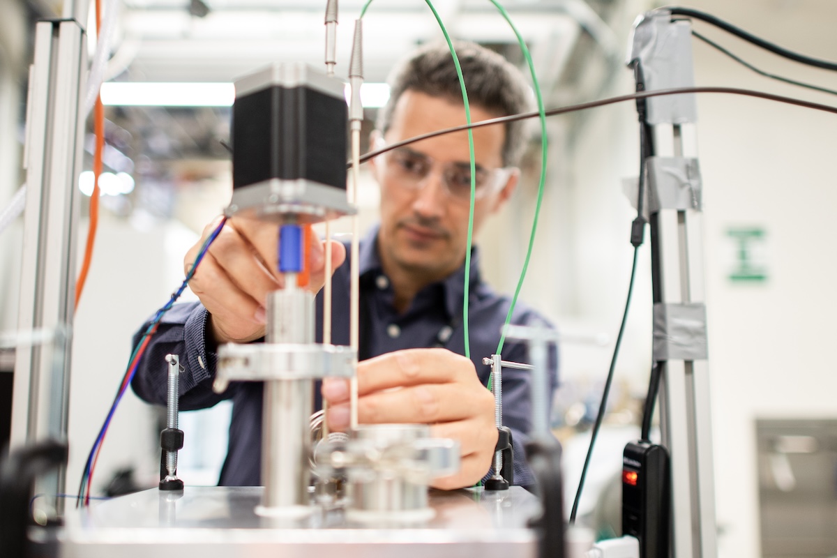 A man out of focus in the background adjusting a piece of laboratory equipment shown in the foreground.